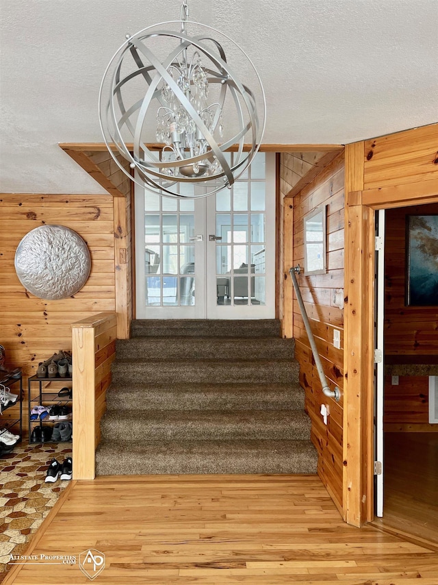 staircase with wood-type flooring, wood walls, a chandelier, and a textured ceiling