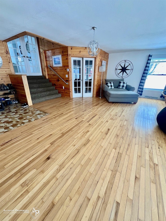 living room with french doors, light hardwood / wood-style flooring, wood walls, and a notable chandelier