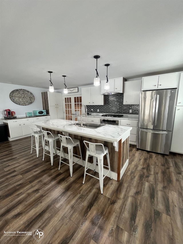 kitchen with white cabinetry, sink, hanging light fixtures, stainless steel refrigerator, and a center island with sink