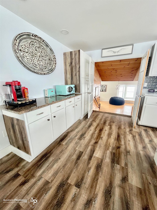 interior space with hardwood / wood-style floors, white cabinets, lofted ceiling, and dark stone countertops