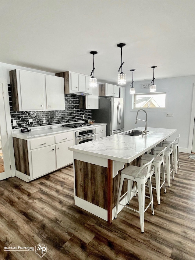 kitchen featuring a center island with sink, stainless steel appliances, white cabinets, and decorative light fixtures