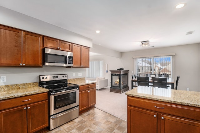 kitchen featuring light stone countertops, light colored carpet, and appliances with stainless steel finishes