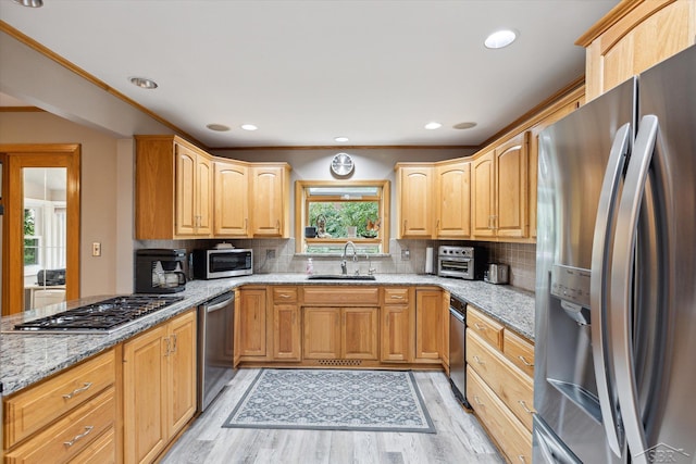 kitchen featuring light stone countertops, light wood-type flooring, appliances with stainless steel finishes, and sink