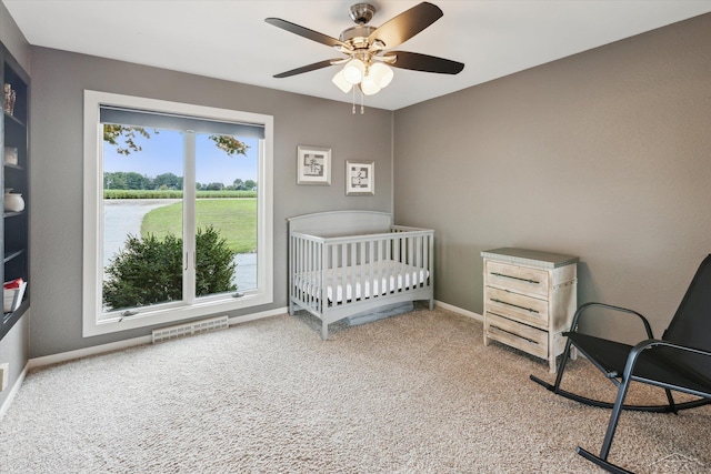 bedroom with ceiling fan, a nursery area, and carpet flooring