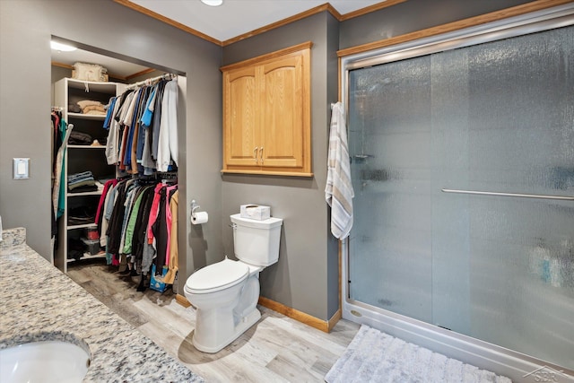 bathroom featuring toilet, hardwood / wood-style flooring, a shower with door, crown molding, and vanity