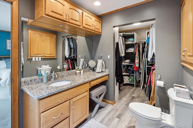 bathroom with toilet, vanity, wood-type flooring, and ornamental molding