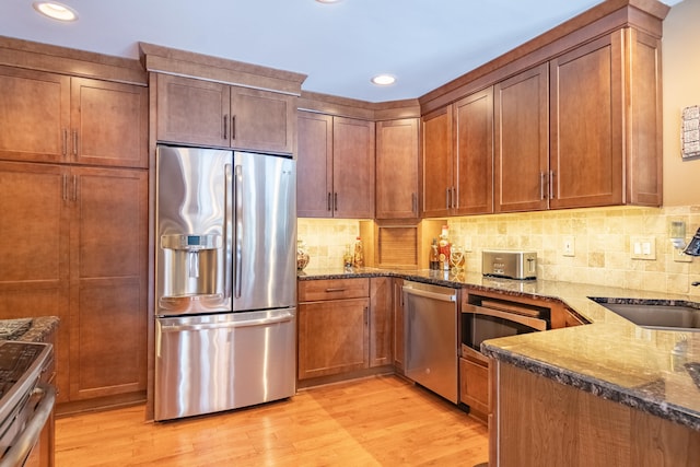 kitchen featuring sink, stainless steel appliances, dark stone counters, and light wood-type flooring