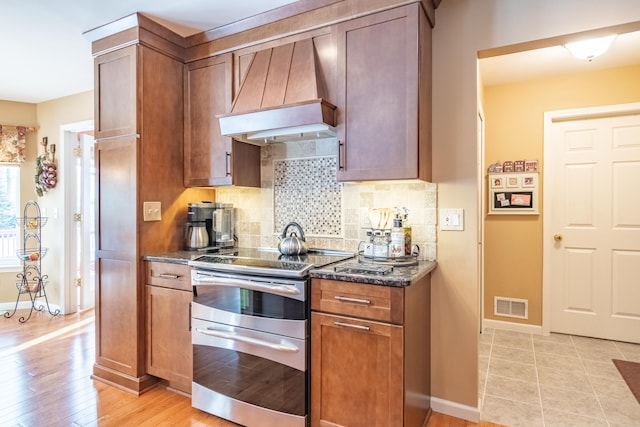 kitchen featuring dark stone counters, custom exhaust hood, range with two ovens, and tasteful backsplash