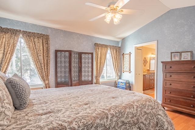 bedroom with light wood-type flooring, connected bathroom, vaulted ceiling, and ceiling fan