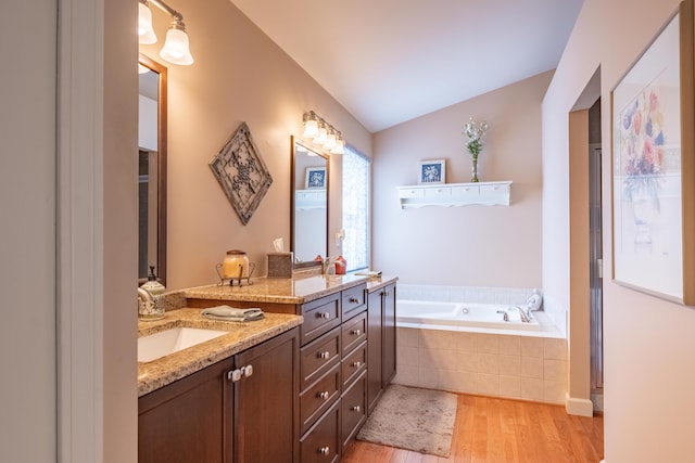 bathroom with wood-type flooring, tiled tub, lofted ceiling, and vanity