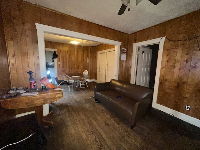 living room featuring dark wood-type flooring, a textured ceiling, and wooden walls