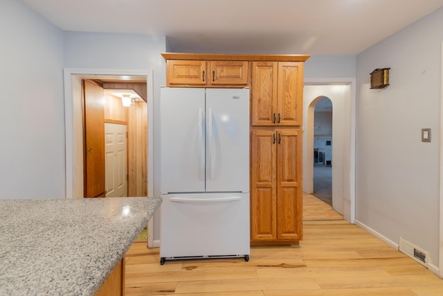 kitchen featuring light stone countertops, white refrigerator, and light hardwood / wood-style floors