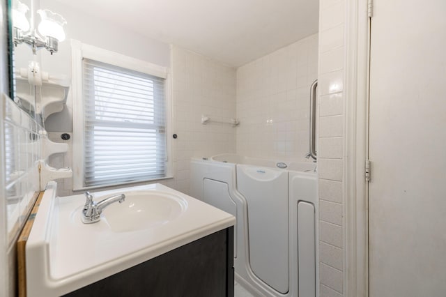 bathroom with an inviting chandelier, washer / clothes dryer, a tub to relax in, and vanity