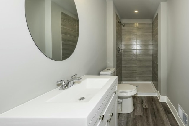 bathroom with toilet, hardwood / wood-style floors, tiled shower, and vanity