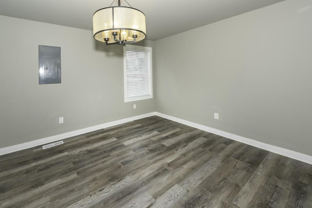 empty room featuring dark hardwood / wood-style floors, a chandelier, and electric panel