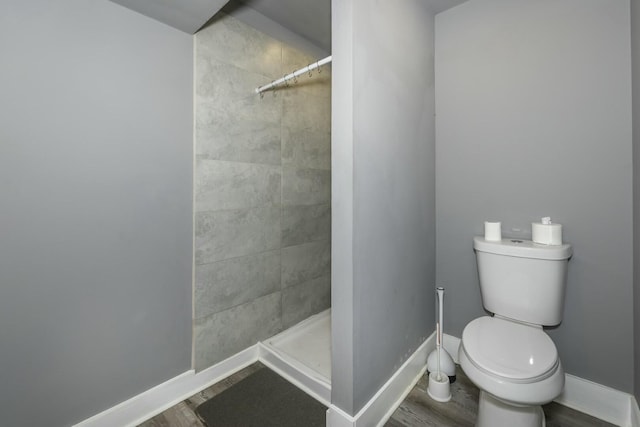 bathroom featuring hardwood / wood-style flooring, toilet, and tiled shower