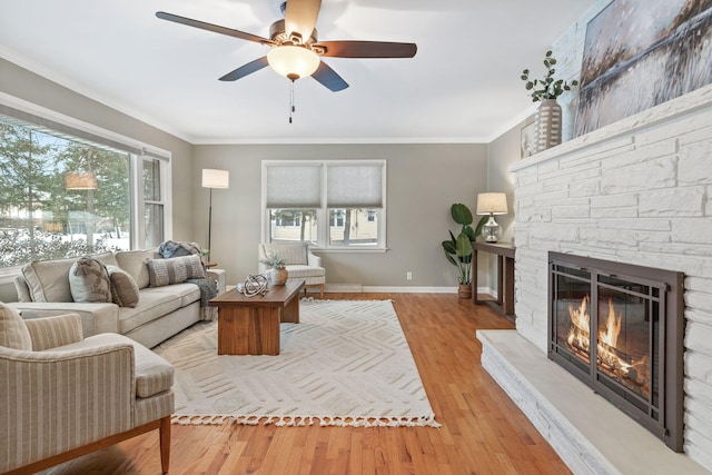 living room featuring ceiling fan, light wood-type flooring, a fireplace, and crown molding