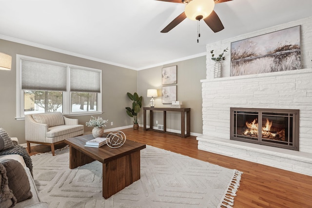 living room with light hardwood / wood-style floors, ornamental molding, ceiling fan, and a fireplace