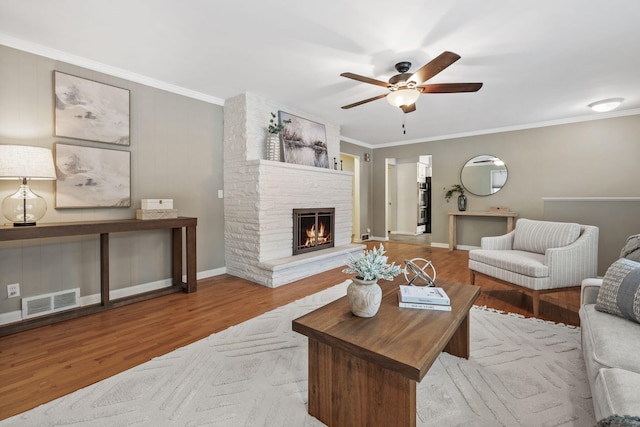 living room with ceiling fan, a fireplace, crown molding, and light hardwood / wood-style floors