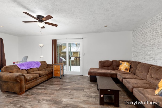 living room featuring ceiling fan, dark hardwood / wood-style flooring, brick wall, and a textured ceiling