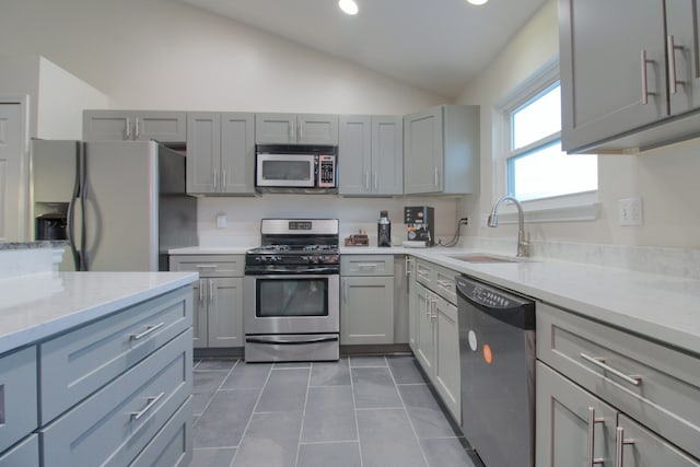 kitchen with sink, gray cabinets, stainless steel appliances, light stone counters, and vaulted ceiling