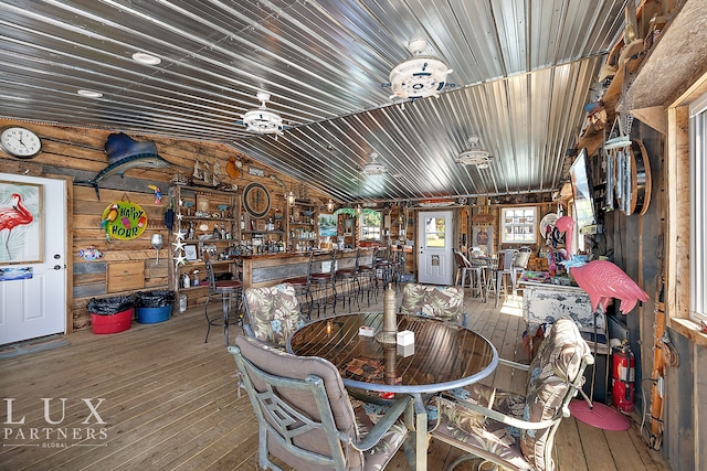 dining space with wood-type flooring, rustic walls, lofted ceiling, and bar area