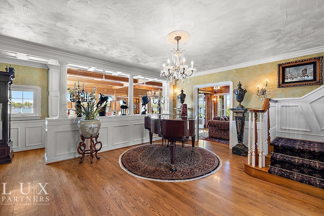 entryway featuring light hardwood / wood-style floors, ornamental molding, ornate columns, and a notable chandelier