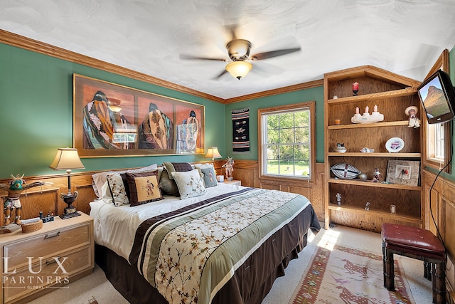 carpeted bedroom featuring wood walls, ceiling fan, and ornamental molding