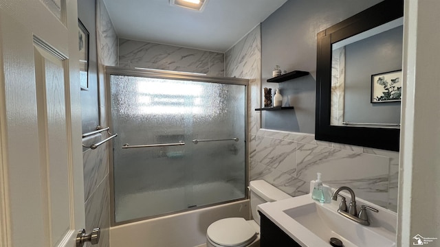 full bathroom with toilet, tile walls, vanity, and shower / bath combination with glass door