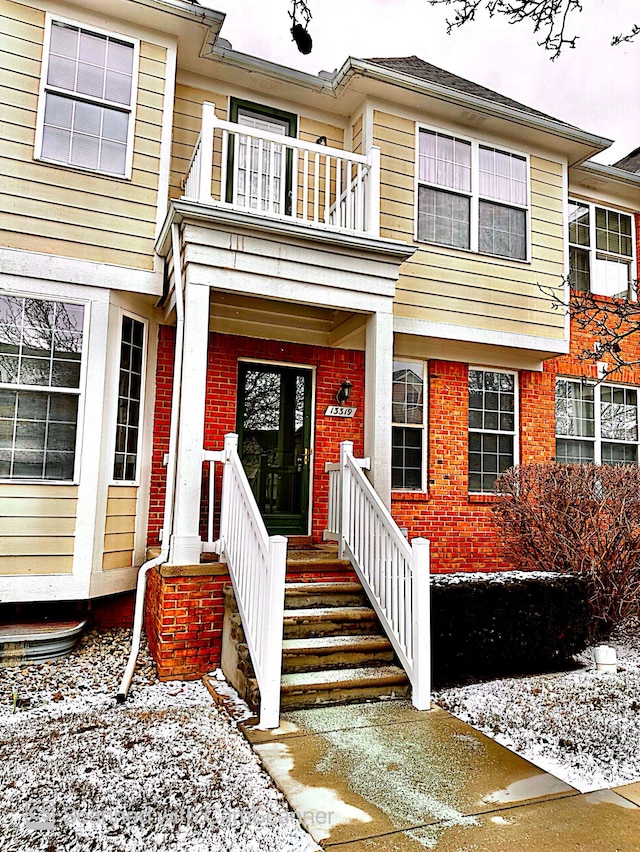 snow covered property entrance with brick siding and a balcony