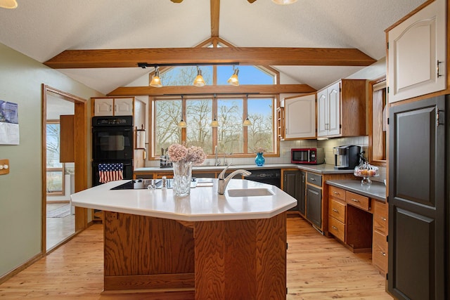 kitchen featuring an island with sink, backsplash, lofted ceiling with beams, black appliances, and sink