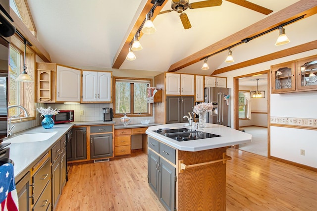 kitchen with an island with sink, backsplash, light wood-type flooring, black appliances, and sink