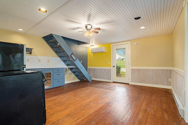 unfurnished office featuring ceiling fan, baseboard heating, hardwood / wood-style floors, and a wall unit AC