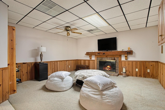 living room with light carpet, ceiling fan, a fireplace, and a drop ceiling