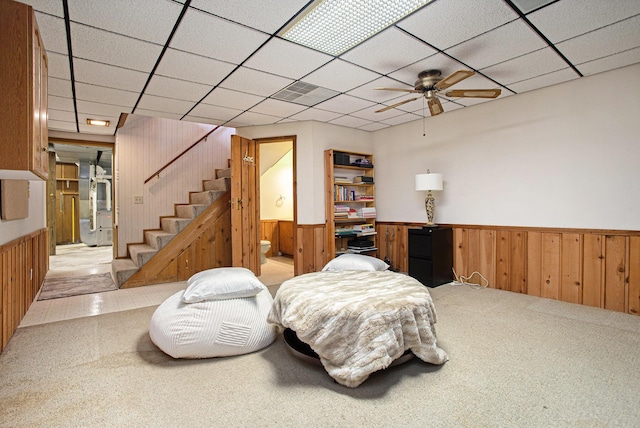 sitting room with ceiling fan, light colored carpet, a paneled ceiling, and wooden walls