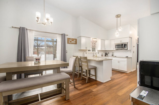 dining room with a chandelier, sink, light hardwood / wood-style flooring, and high vaulted ceiling