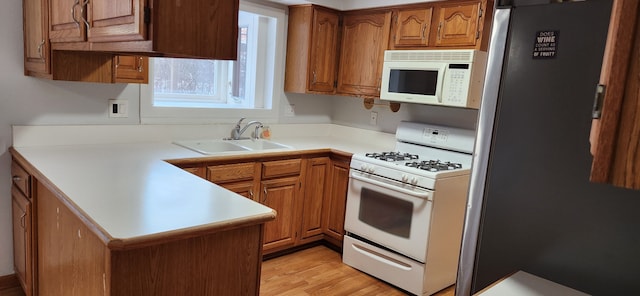 kitchen with kitchen peninsula, sink, light hardwood / wood-style flooring, and white appliances