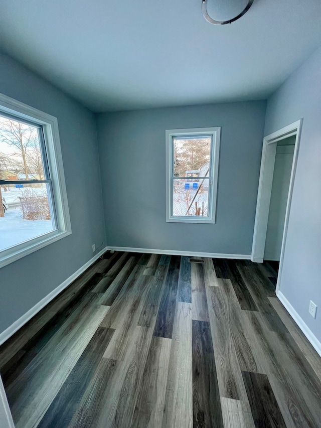 unfurnished bedroom featuring a closet, multiple windows, and dark hardwood / wood-style floors