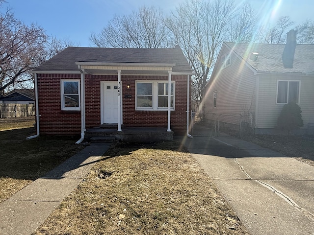 bungalow with brick siding, covered porch, roof with shingles, and fence