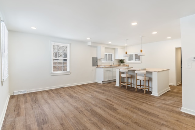 kitchen featuring a center island, pendant lighting, a kitchen bar, white cabinetry, and light wood-type flooring