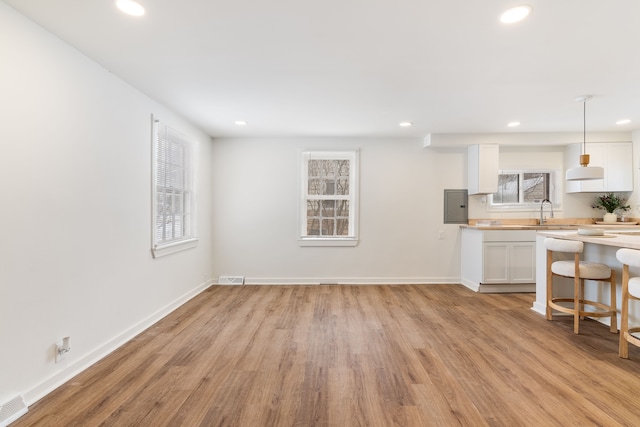 kitchen featuring white cabinetry, decorative light fixtures, electric panel, light hardwood / wood-style flooring, and sink