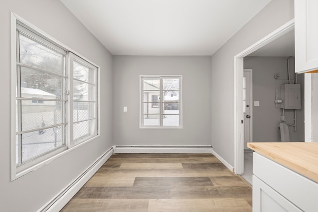 unfurnished dining area featuring a baseboard heating unit, a healthy amount of sunlight, and light wood-type flooring