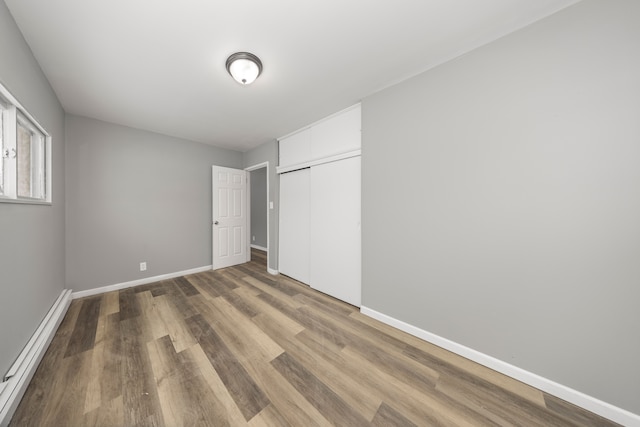 unfurnished bedroom featuring baseboard heating, a closet, and hardwood / wood-style floors