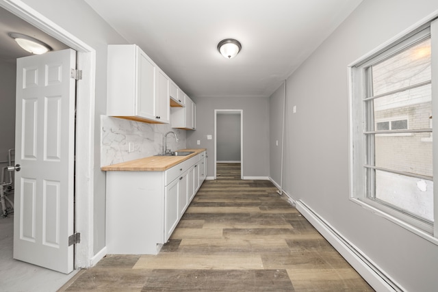 kitchen with tasteful backsplash, butcher block countertops, sink, white cabinetry, and a baseboard radiator