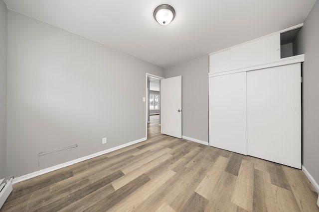 unfurnished bedroom featuring baseboard heating, a closet, and light hardwood / wood-style floors