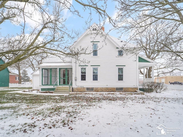 snow covered back of property with a sunroom