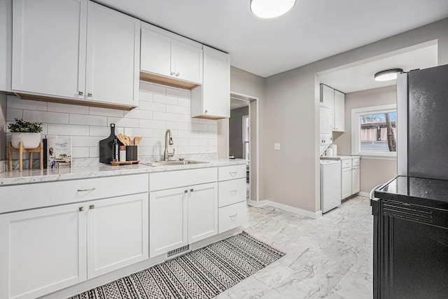 kitchen with white cabinets, washer / dryer, sink, backsplash, and stainless steel fridge