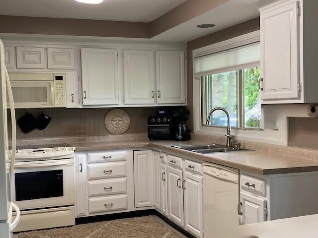 kitchen featuring white cabinetry, sink, and white appliances