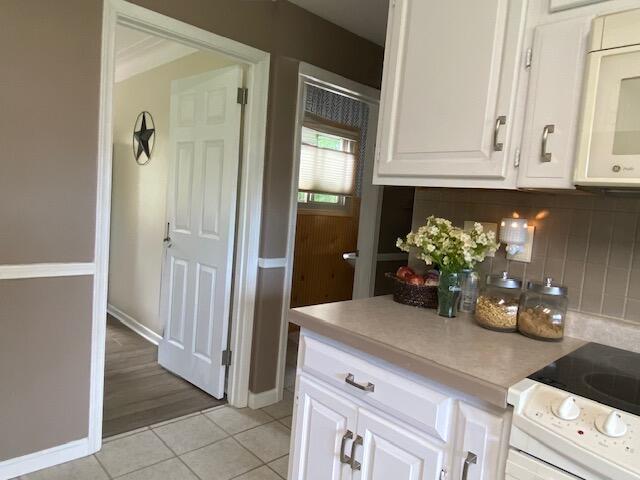 kitchen featuring light tile patterned flooring, electric range, white cabinets, and tasteful backsplash