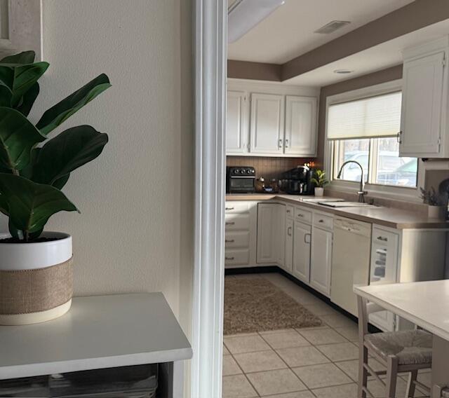 kitchen featuring dishwasher, white cabinetry, sink, backsplash, and light tile patterned flooring